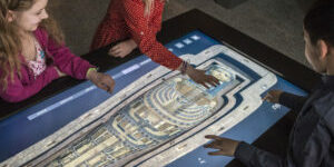 Three kids using a large touch table to look at a 3D scan of a sarcophagus